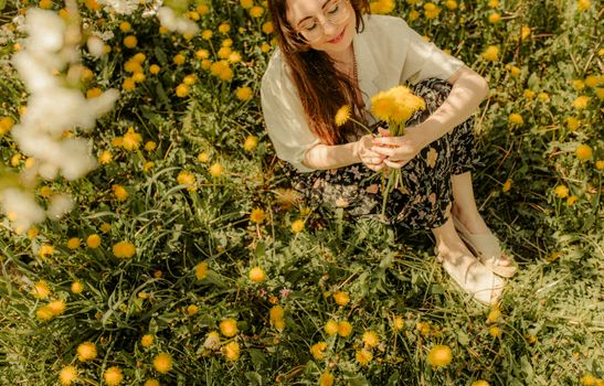 Woman with long brown hair smiling while holding yellow flowers in a meadow.