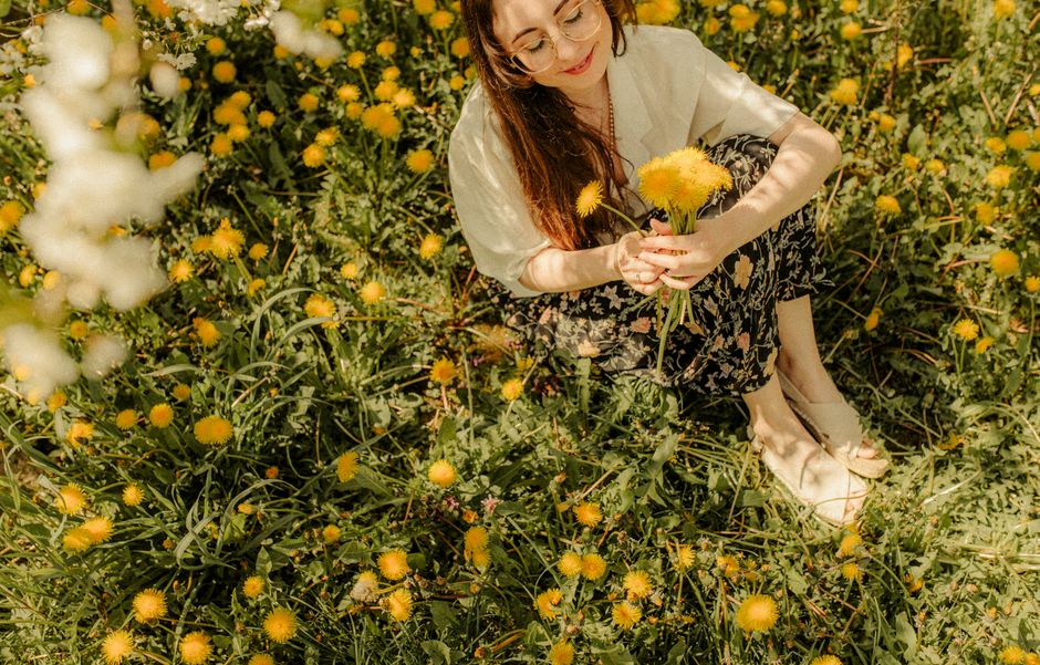 Woman with long brown hair smiling while holding yellow flowers in a meadow.