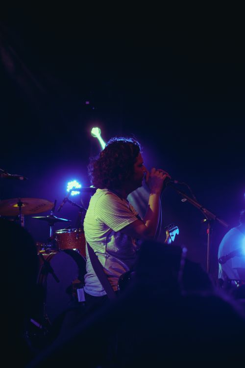 Free Energetic live performance featuring a singer and guitarist on stage under vibrant lights. Stock Photo