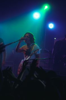 Musician on stage playing guitar and singing during a vibrant concert performance.