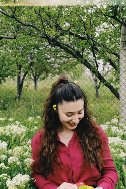 Smiling Woman in Red Shirt Sitting among Flowers
