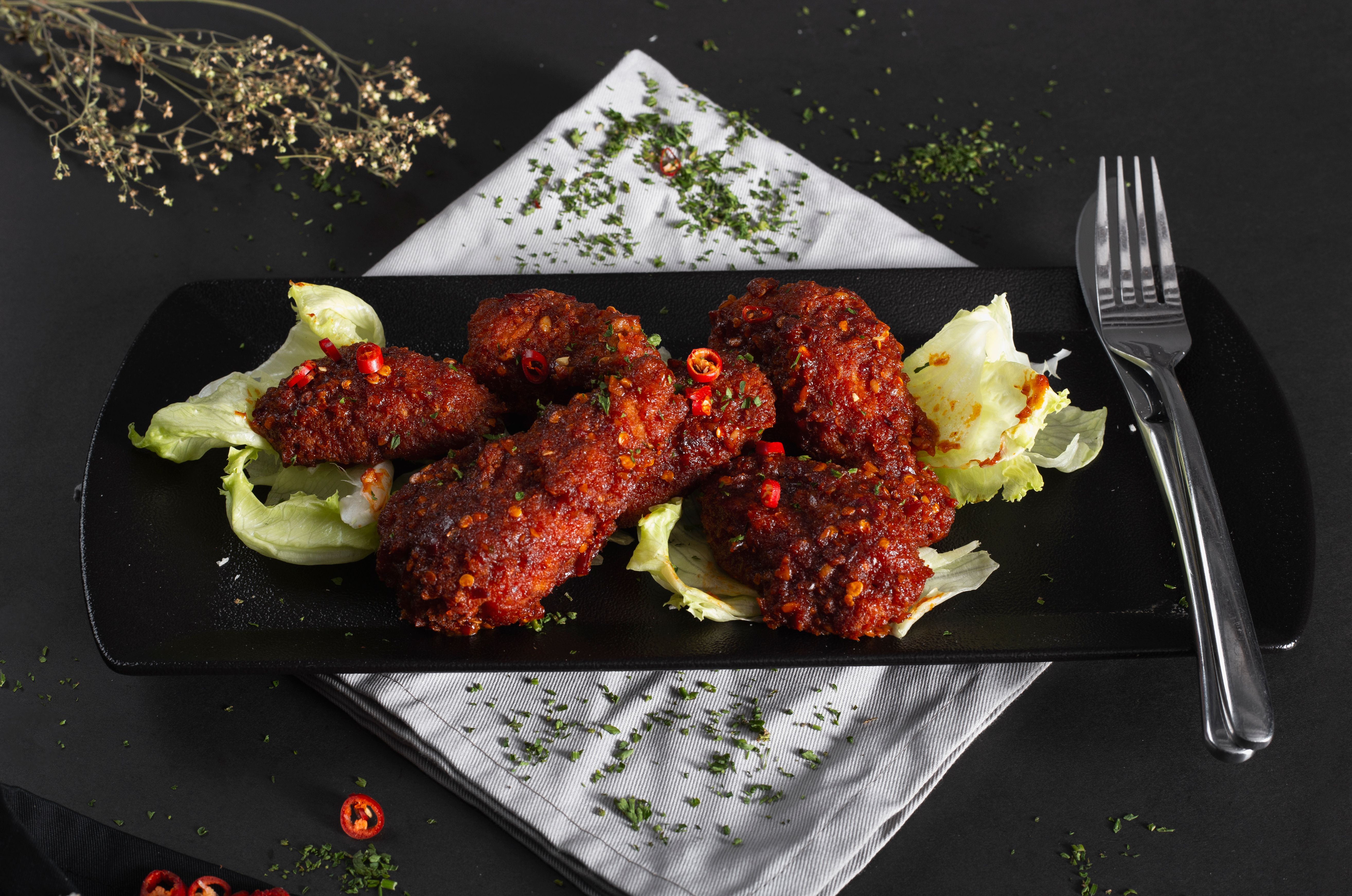 Close-up of spicy fried chicken wings on a dark plate, garnished with lettuce and herbs.