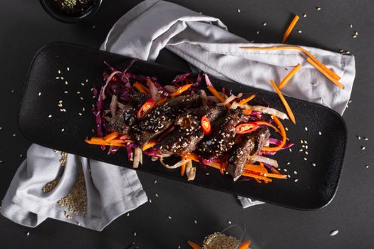 Delicious Asian-style beef salad with sesame seeds and colorful veggies on a black plate.