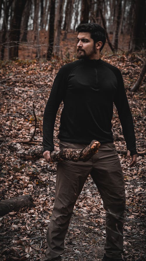 Bearded Man in Black Sweater Standing in Woods with Branch in Hands