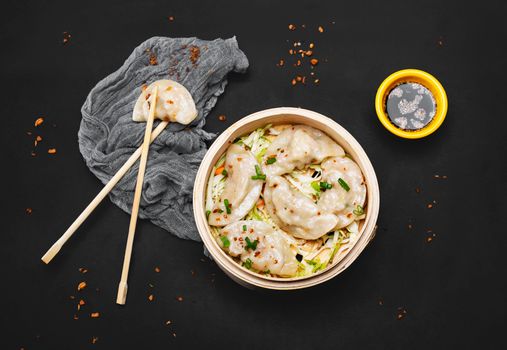 Top view of steamed dumplings with chopsticks and soy dipping sauce on a black background.