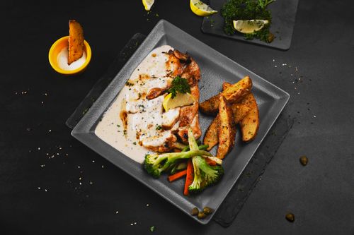 Free Grilled fish served with creamy sauce, veggies, and wedge potatoes on a slate plate. Stock Photo