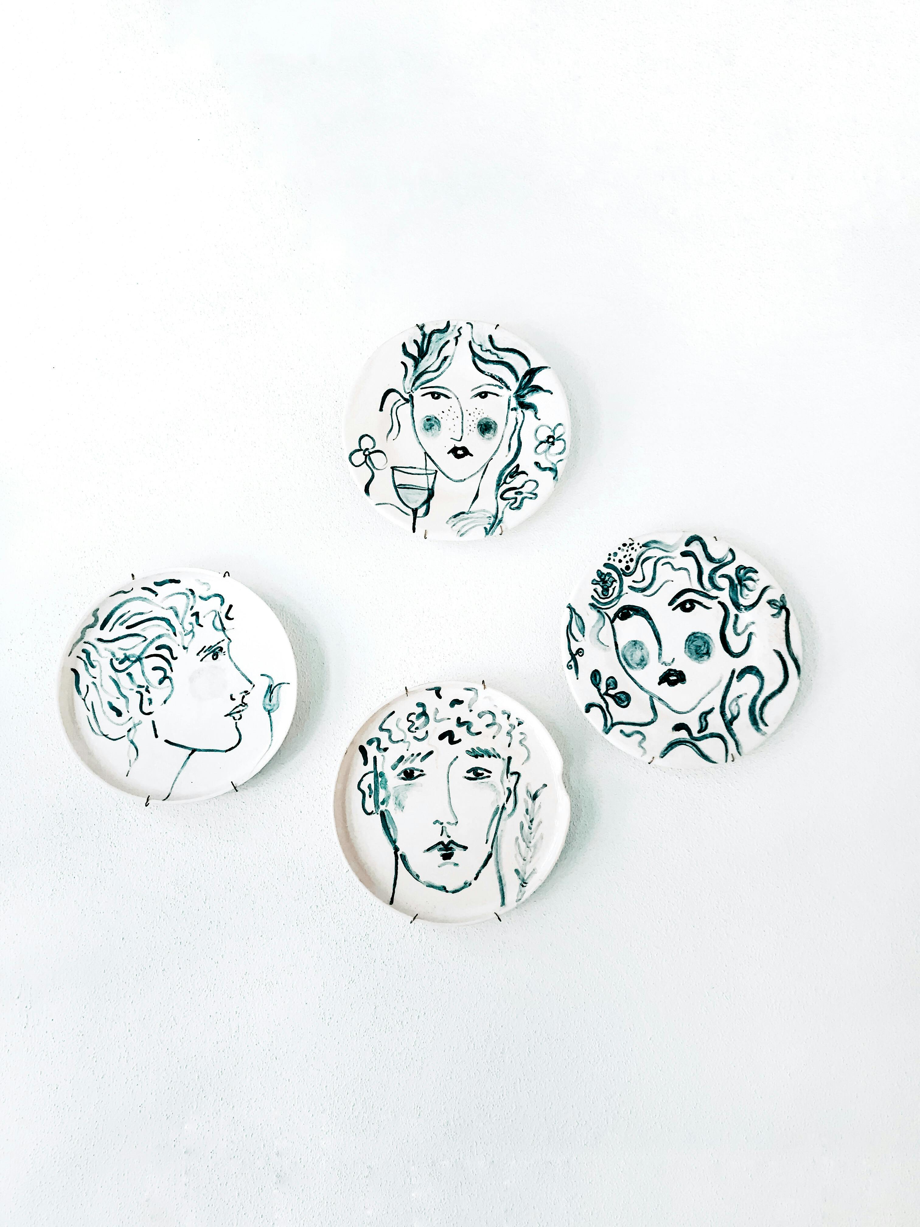 Minimalist ceramic plates with abstract face designs on a white background, featuring decorative art.