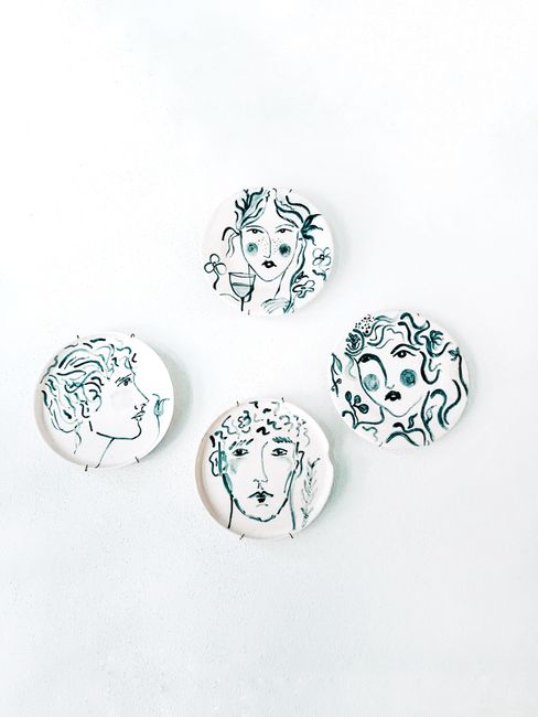 Minimalist ceramic plates with abstract face designs on a white background, featuring decorative art.