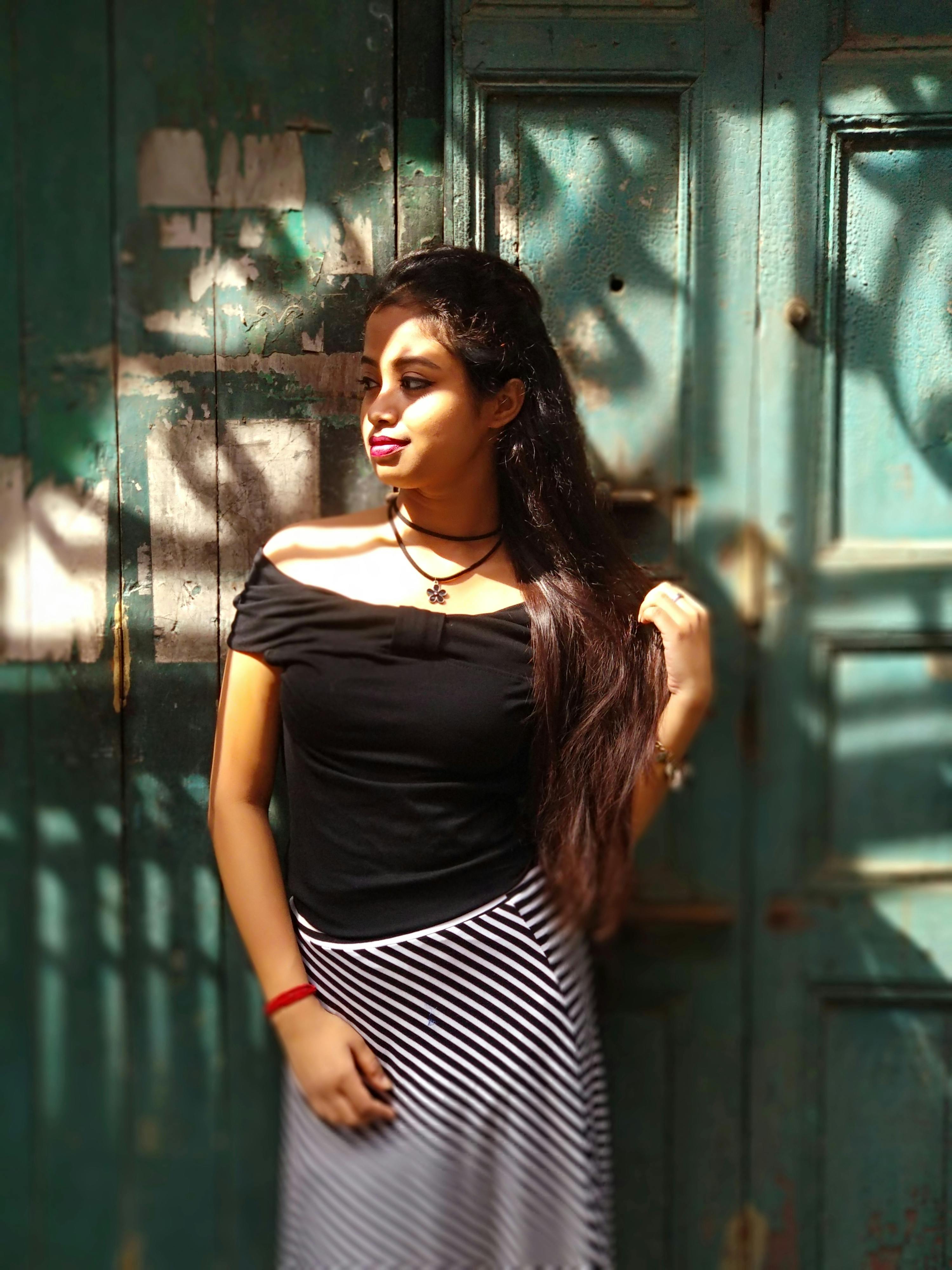 Woman posing by a vintage door in sunlight, highlighting fashion style.