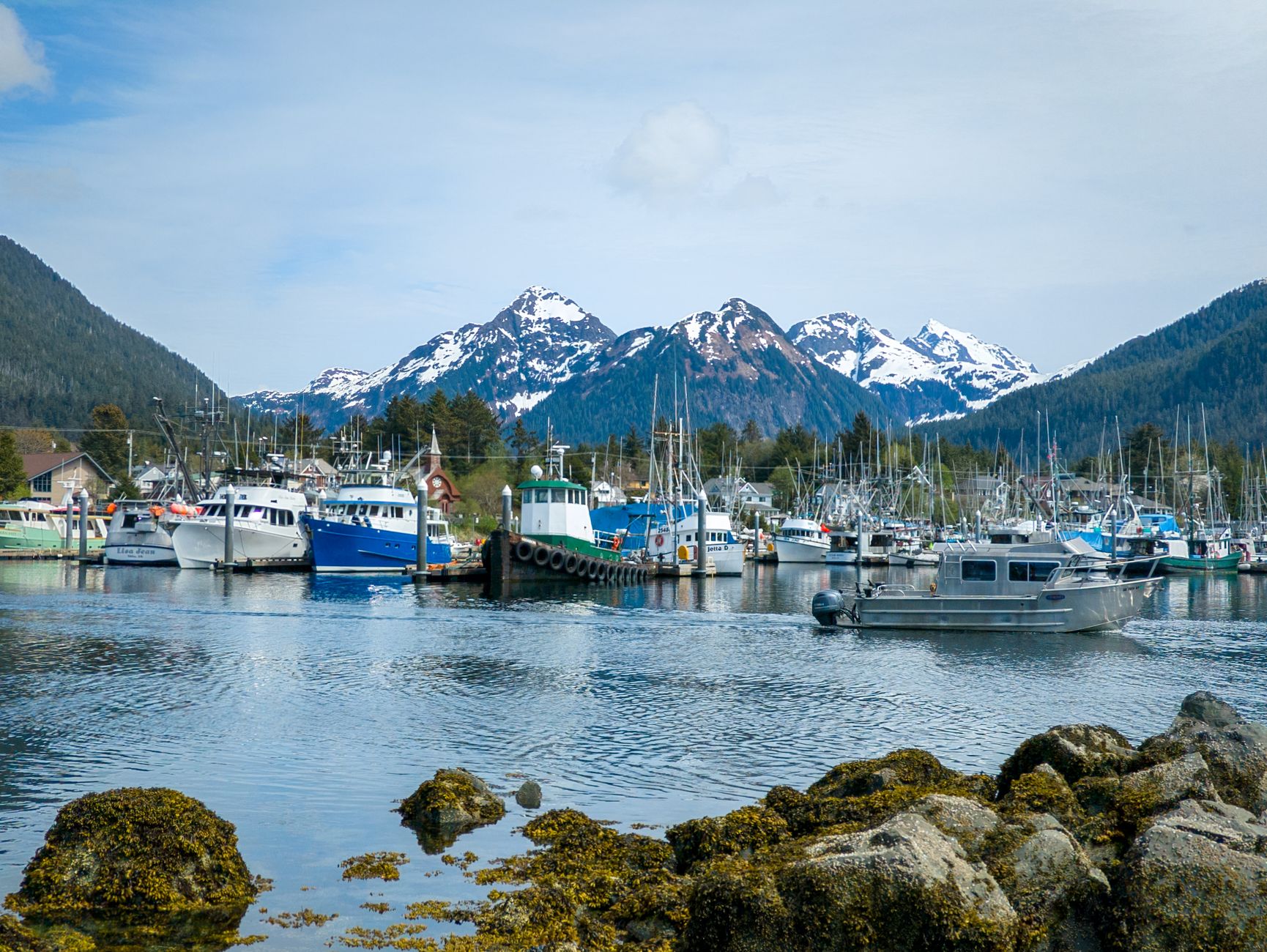 Picturesque harbor with boats, mountains, and clear skies in Sitka, Alaska, near the water's edge.