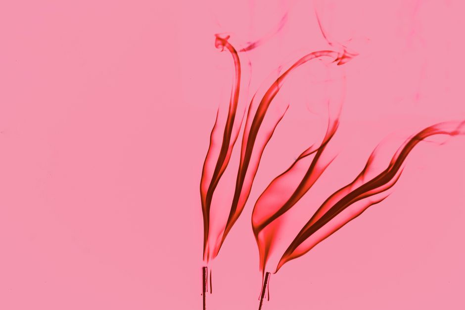 Vibrant red smoke swirls elegantly against a soft pink background, creating artistic abstract shapes.