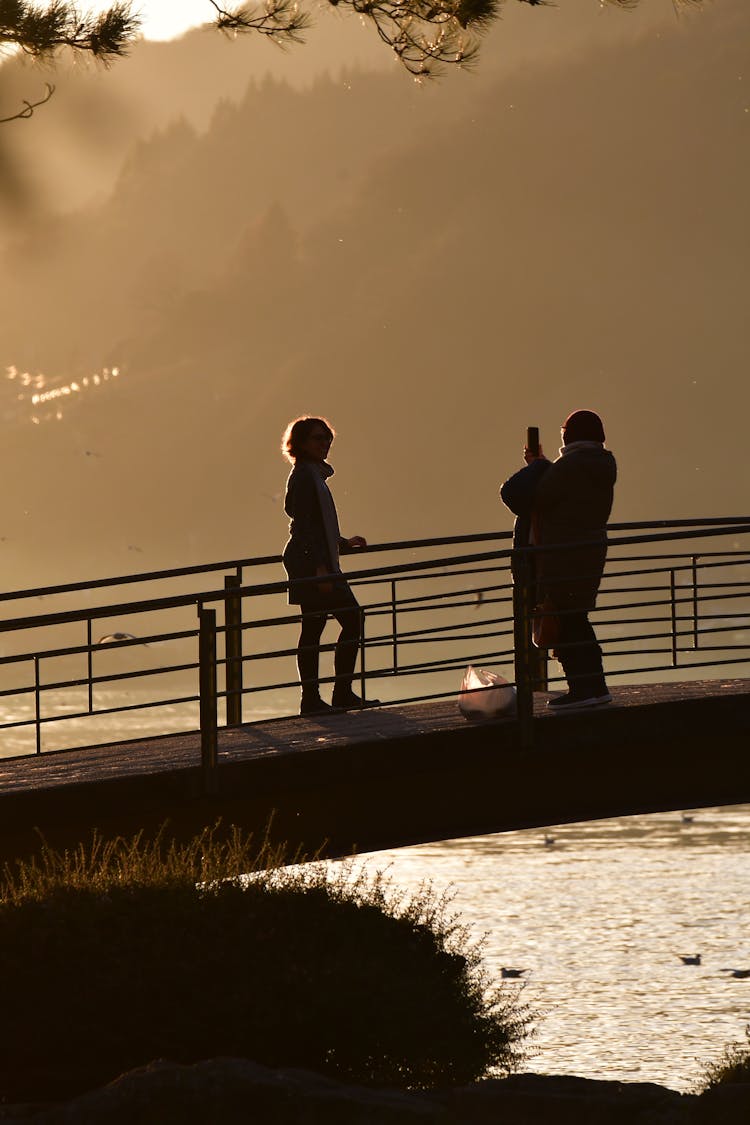 Silhouette Of People Taking Pictures On Bridge At Sunset