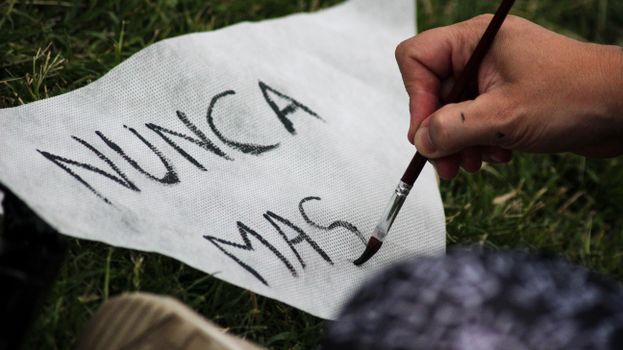 A person painting 'Nunca Más' on fabric, symbolizing a protest for justice and remembrance.