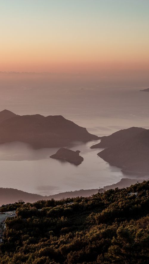 Free A breathtaking view of a mountain range and coastline at sunset, enveloped in soft mist. Stock Photo
