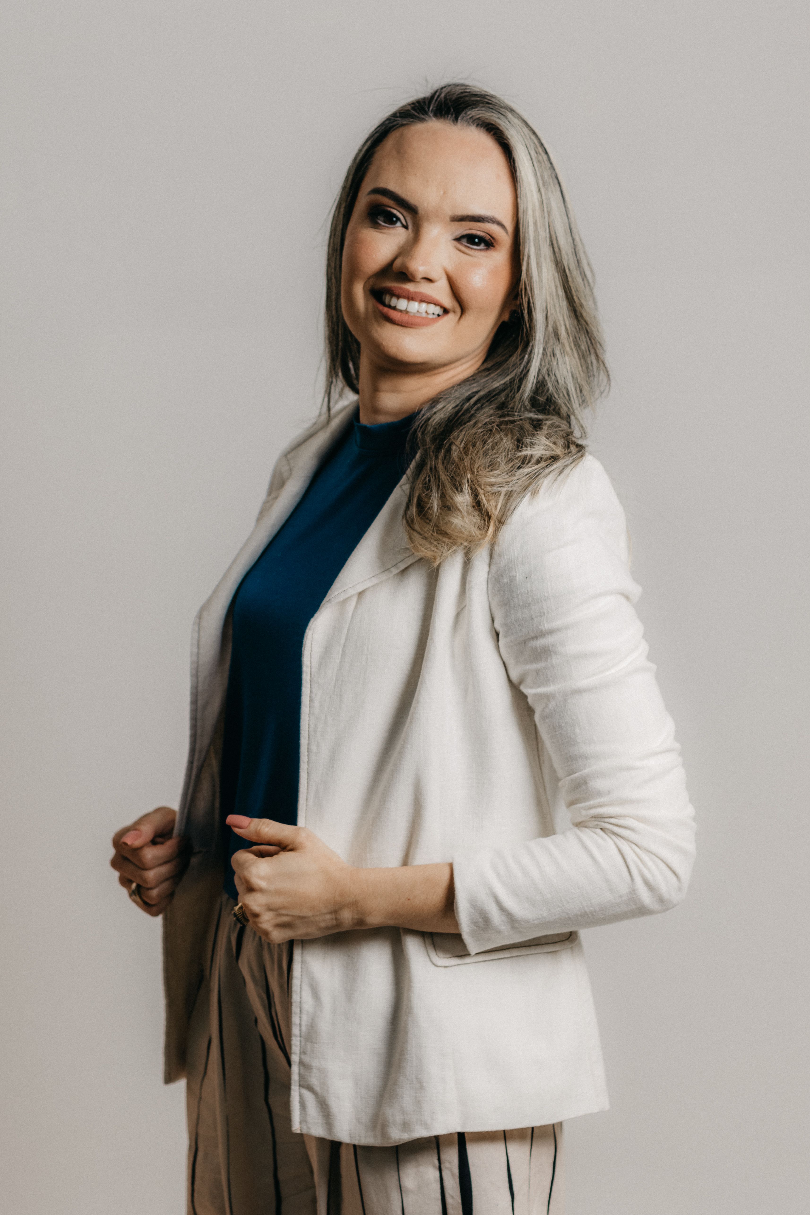 Fashionable woman in a white jacket and striped pants smiling confidently in an indoor photoshoot.