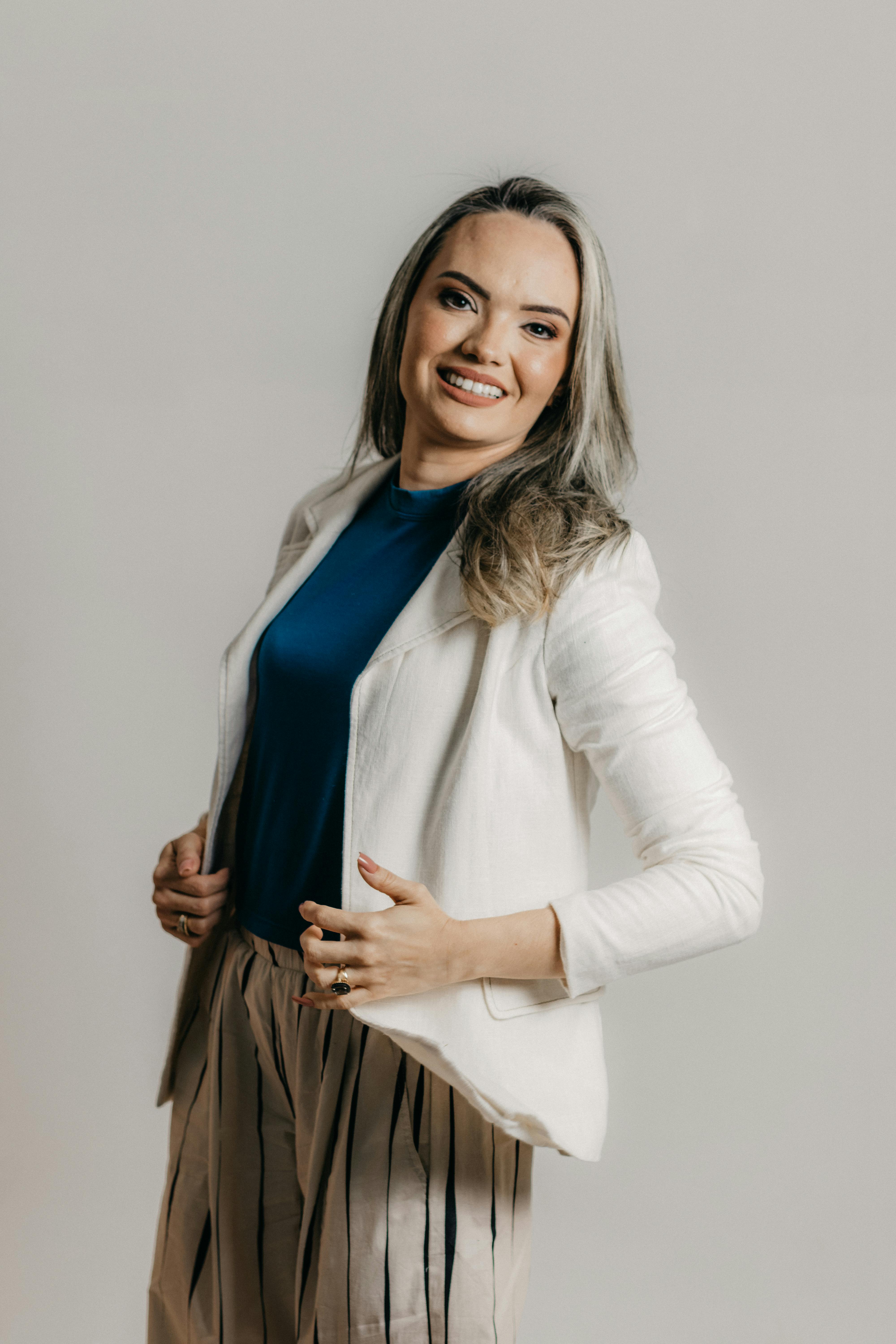 Charming businesswoman in white jacket smiles confidently in studio setting.