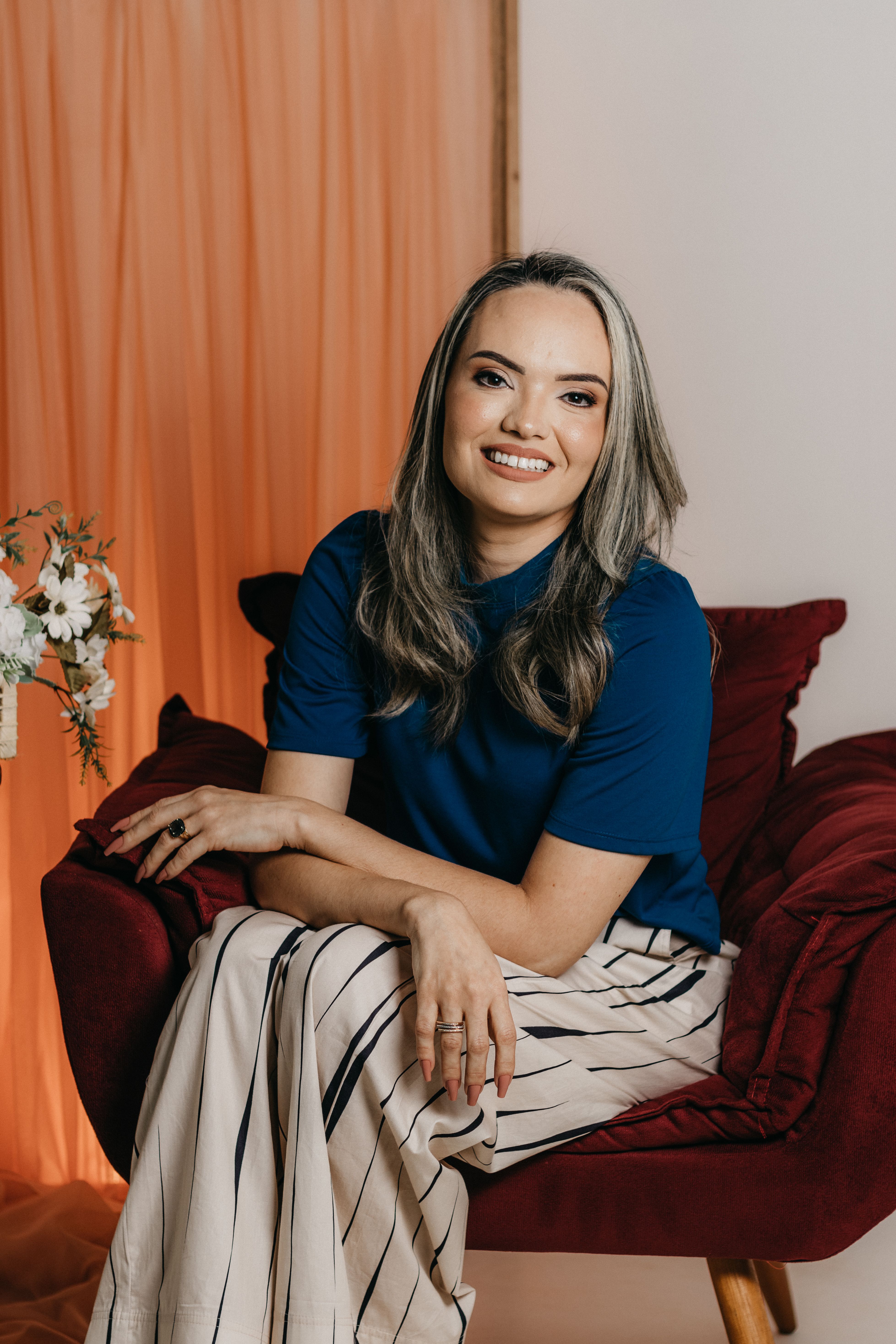 Smiling woman sits elegantly on an armchair in a studio with warm tones.