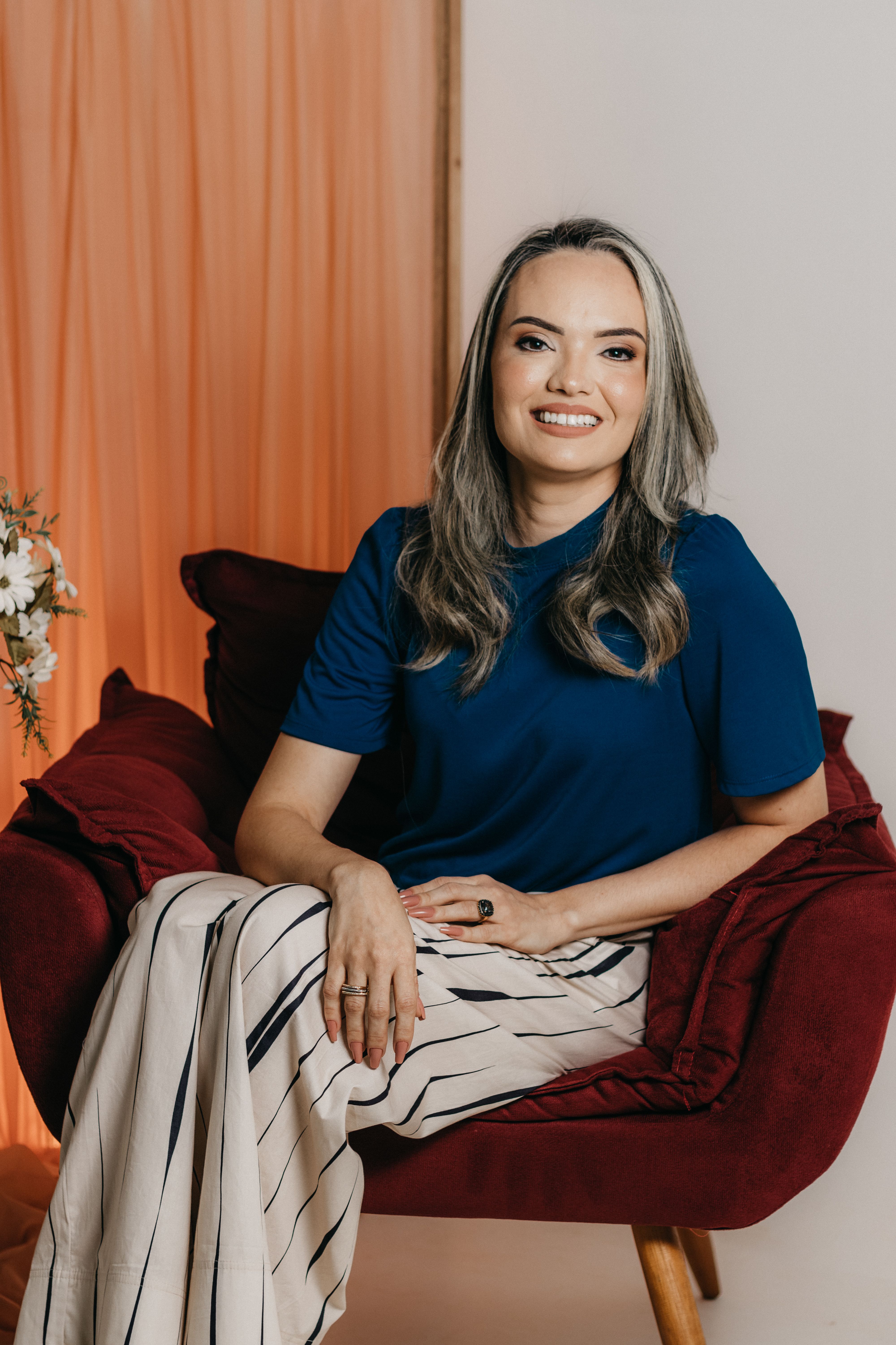 Stylish woman sitting on a red chair posing elegantly in a fashion studio shoot.