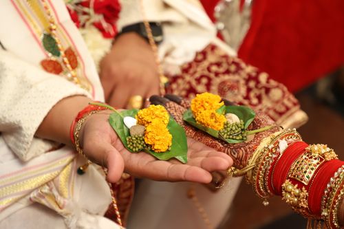 Free Close-up of Indian wedding ritual showing hands holding marigold flowers and betel leaves. Stock Photo
