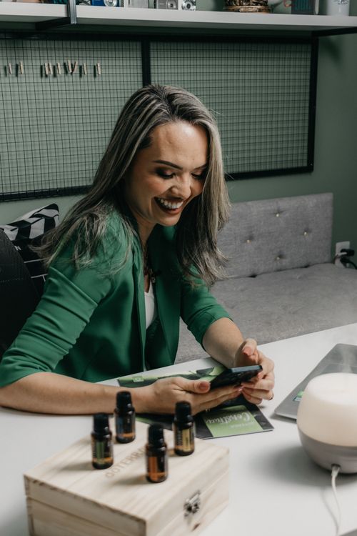 Free Smiling woman using smartphone in modern office with essential oils on desk, exuding elegance and technology. Stock Photo