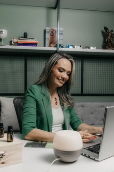 Businesswoman in a green suit using a laptop at her office desk, surrounded by decor.