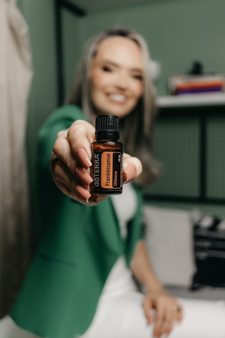 Young Woman Sitting In An Office And Holding A Bottle Of Essential Oil 