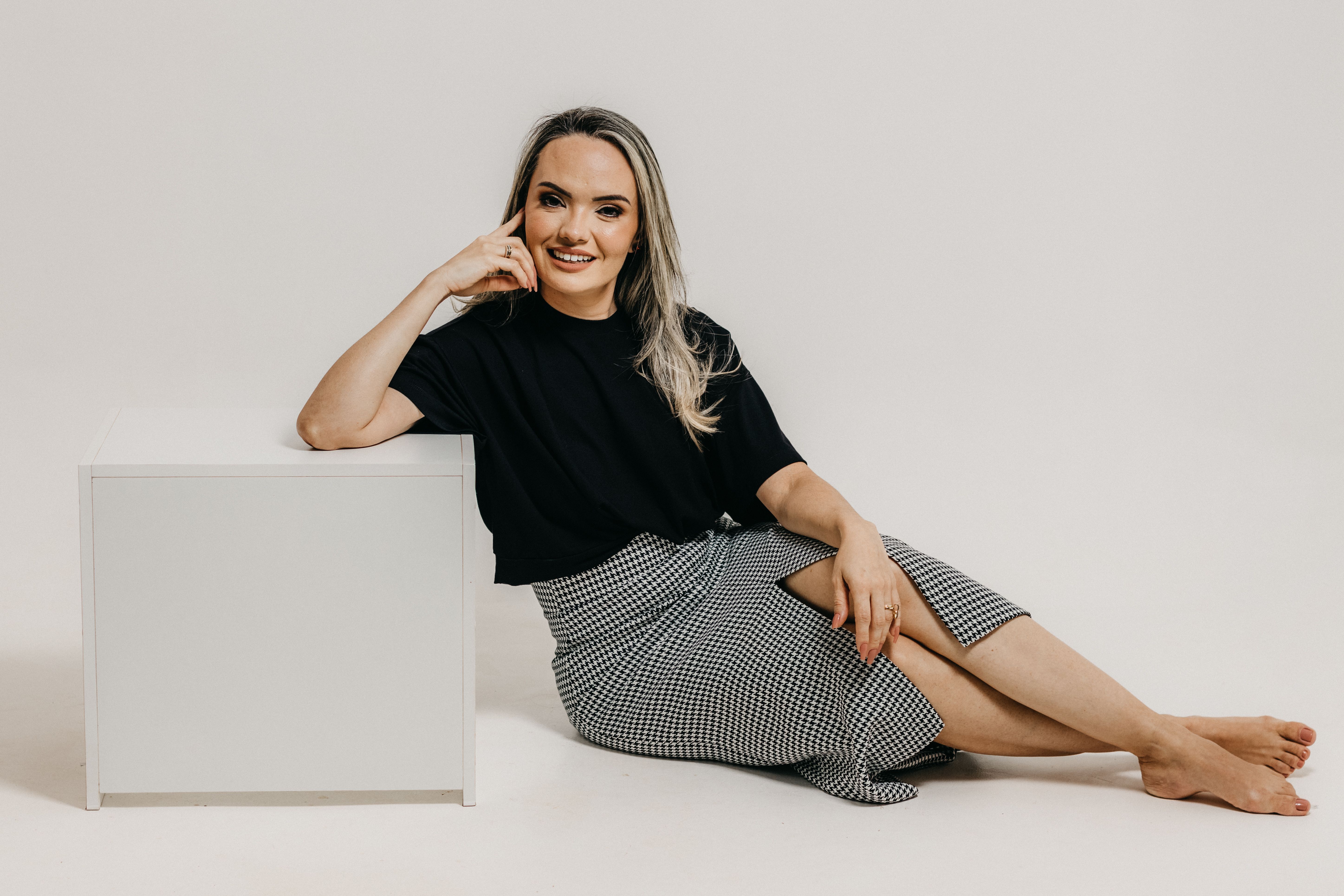 Stylish woman in a black top and checkered skirt posing barefoot in a studio setting.