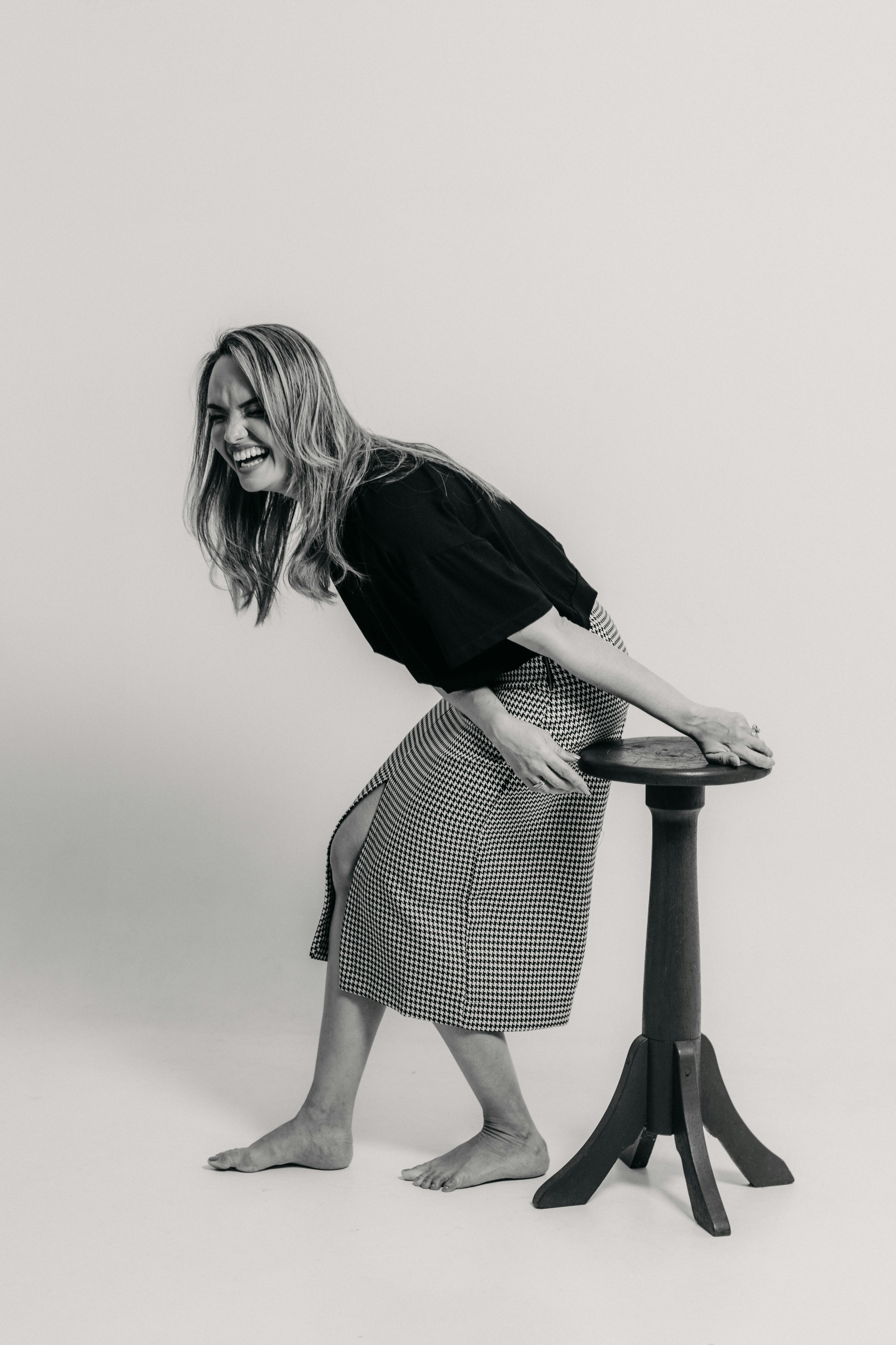 A joyful woman laughing while leaning on a stool, captured in black and white.