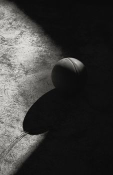 Dramatic black and white image of a basketball casting a shadow on a textured ground.