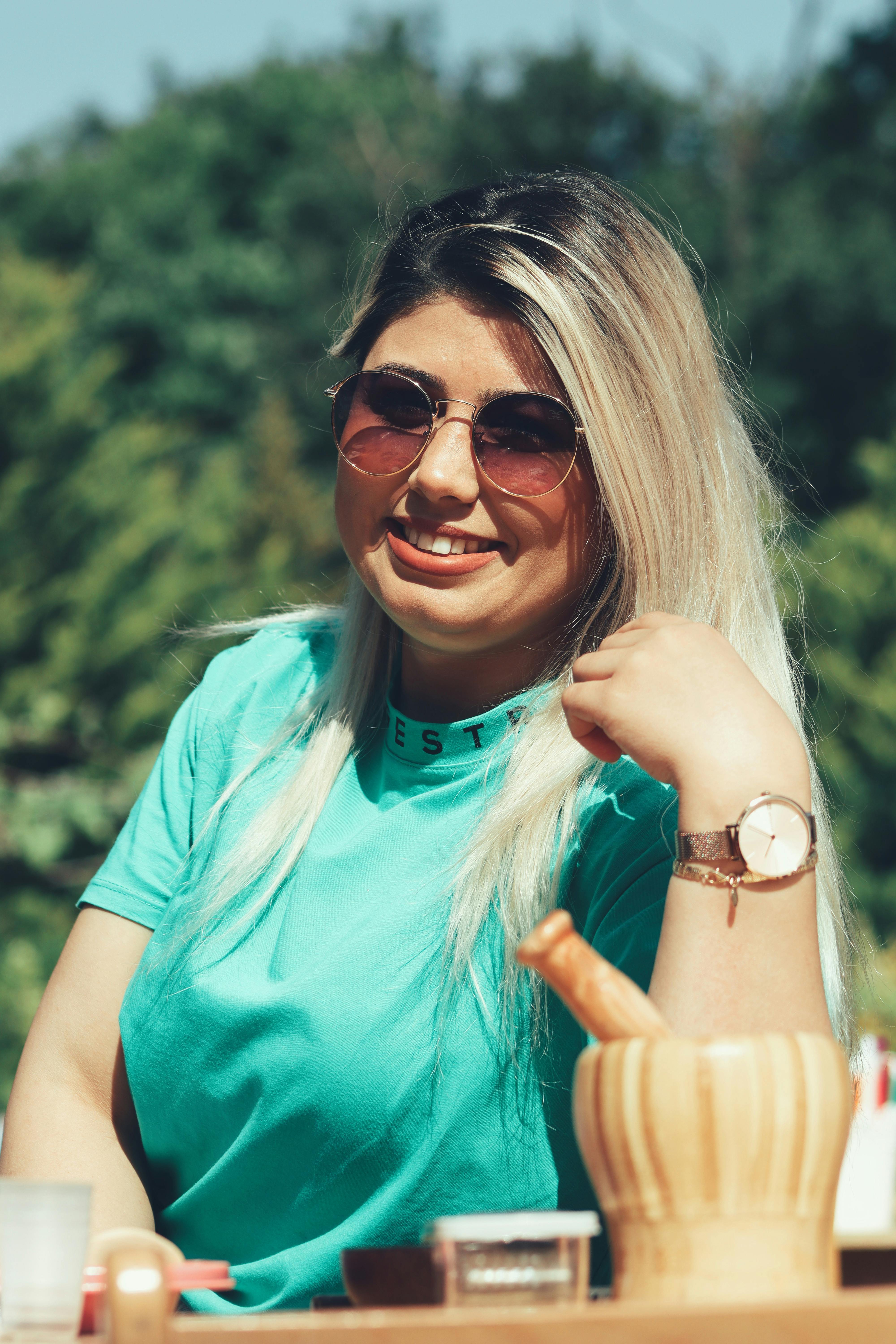 Smiling woman in sunglasses with long blonde hair enjoys a sunny day outdoors.