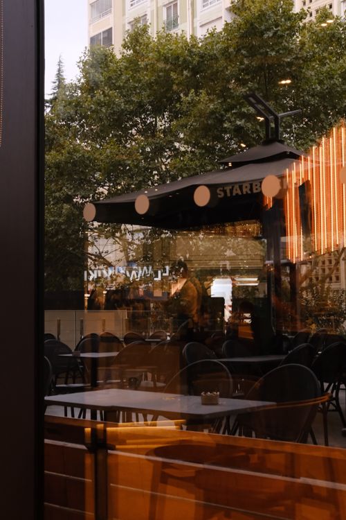 Free Warm urban cafe scene with outdoor seating, reflections, and street ambiance. Stock Photo