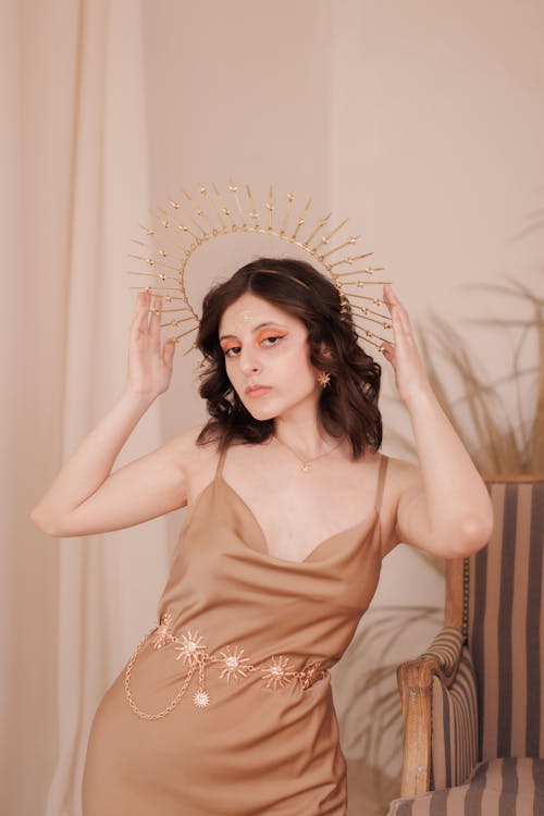 Young Brunette Woman Posing in Light Brown Dress and Golden Sun Halo Headpiece