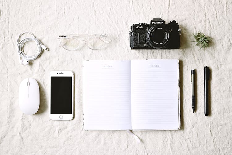 White Notebook Beside Pens And Gold Iphone 6 And Camera