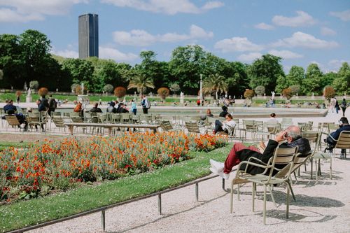 Free People relaxing in Luxembourg Garden, Paris, with vibrant flowers and a tower in the background. Stock Photo