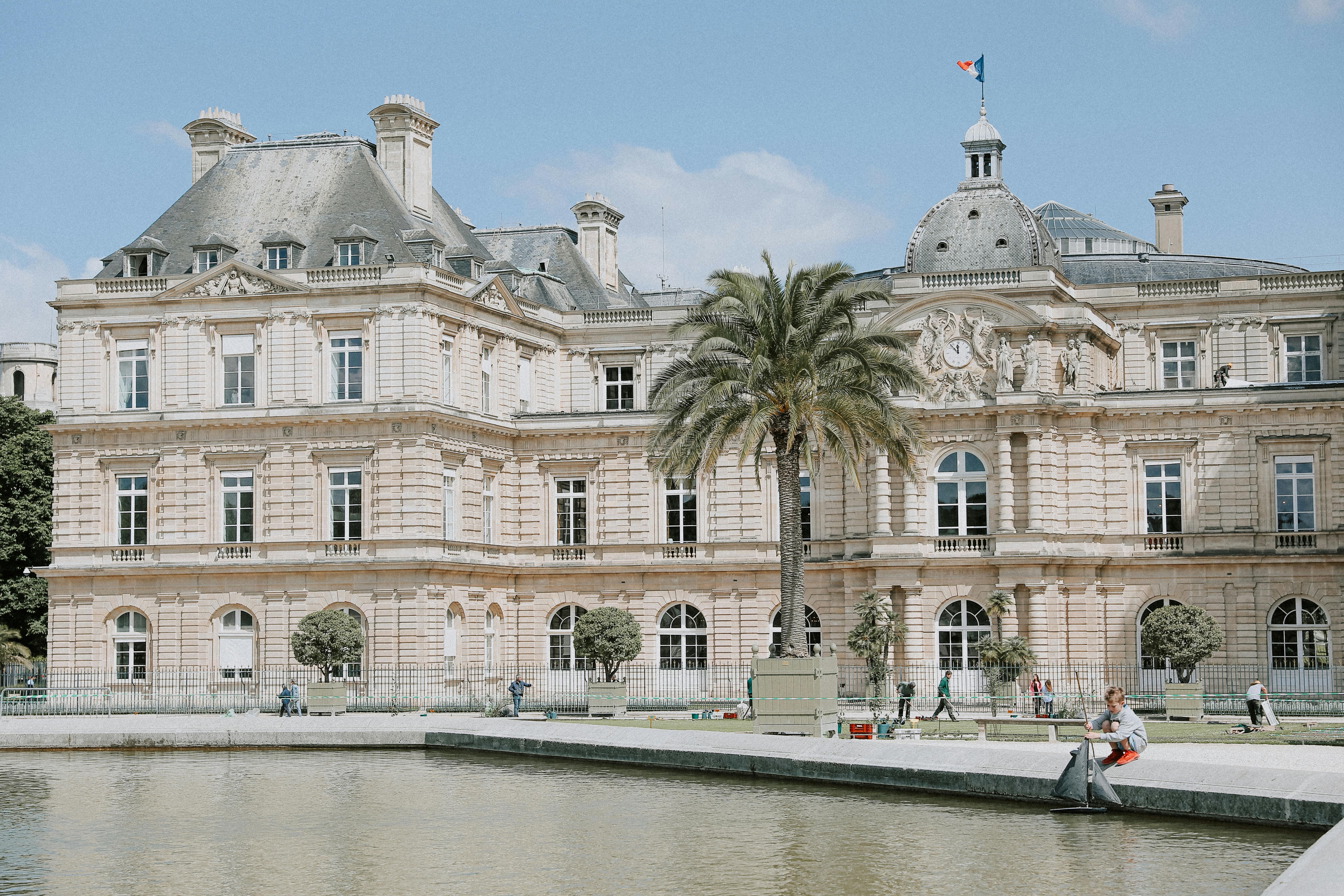 Elegant view of Luxembourg Palace with a foreground pond under a bright daytime sky.