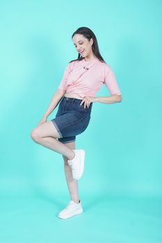 Fashionable woman posing in denim shorts with a pink top on a blue background.