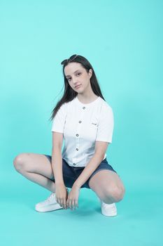 Caucasian woman in casual attire crouching in a studio with a blue backdrop.