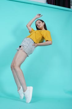 Woman in casual yellow top and denim shorts posing creatively in studio