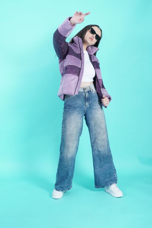 Free Woman in a stylish jacket and jeans confidently poses on a blue backdrop. Stock Photo