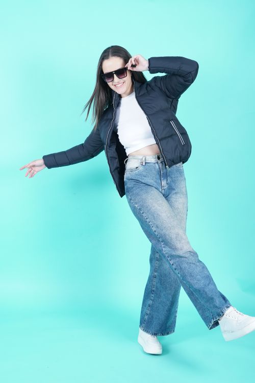 Free Woman in denim jeans and jacket posing confidently against a blue background in a studio shoot. Stock Photo