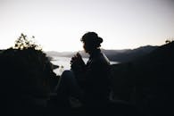 日落时分，一名女子坐在宁静的山间湖畔，身影映照出自然的宁静