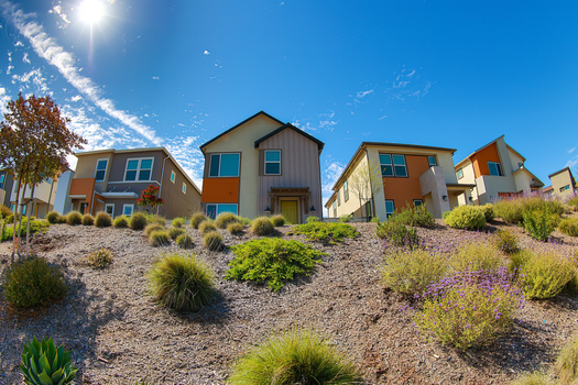 Stunning modern houses with geometric facades under a sunny blue sky, showcasing lush landscaping.