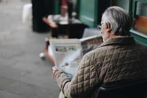 Free Elderly man reading a newspaper in an outdoor cafe setting, enjoying a peaceful moment. Stock Photo