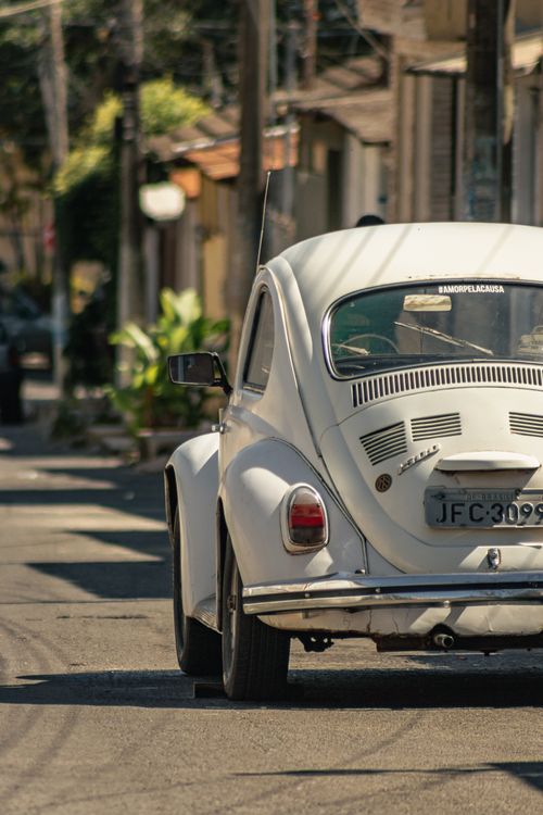 Free A classic white Volkswagen Beetle parked on a sunlit street in Cidade Ocidental, Brazil. Stock Photo