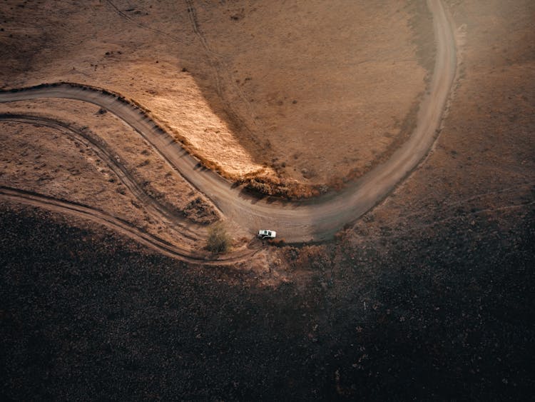 Top View Of A Car Driving On A Road Among Fields With Dry Grass 