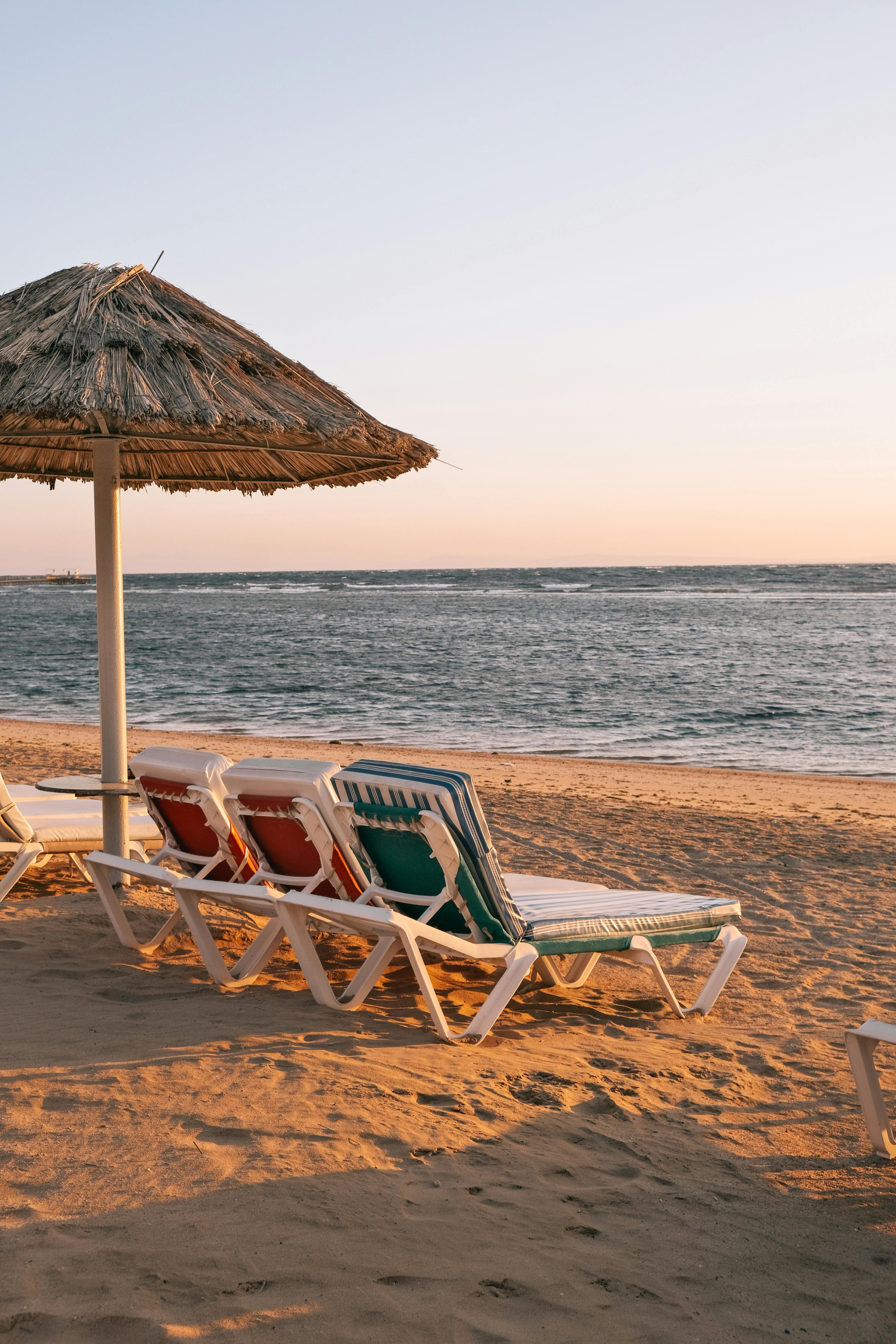 Peaceful beach with sun loungers under a thatched umbrella at sunset along a tranquil shoreline.