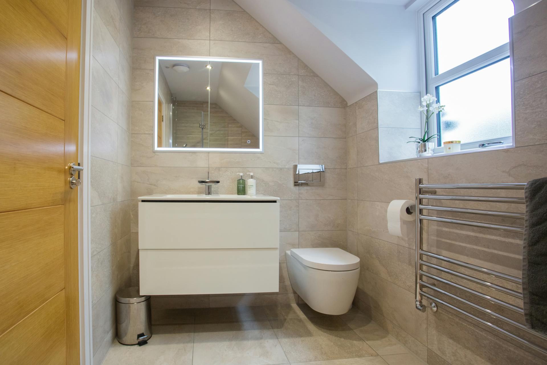 Stylish Colchester bathroom with wall-mounted toilet and illuminated mirror.