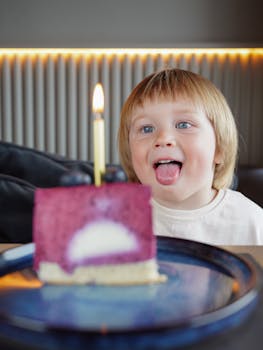 A smiling child eagerly anticipates blowing out a candle on a berry cake.