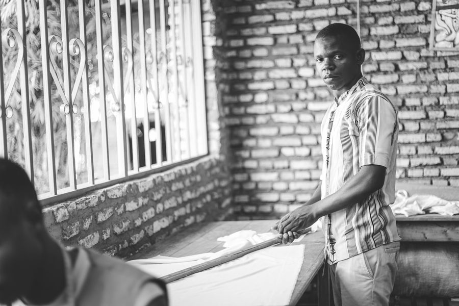 Black and white image of a man ironing clothes indoors with a brick wall background.