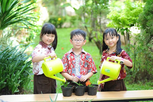 Children Holding Watering Cans and Watering the Plants in the Garden 